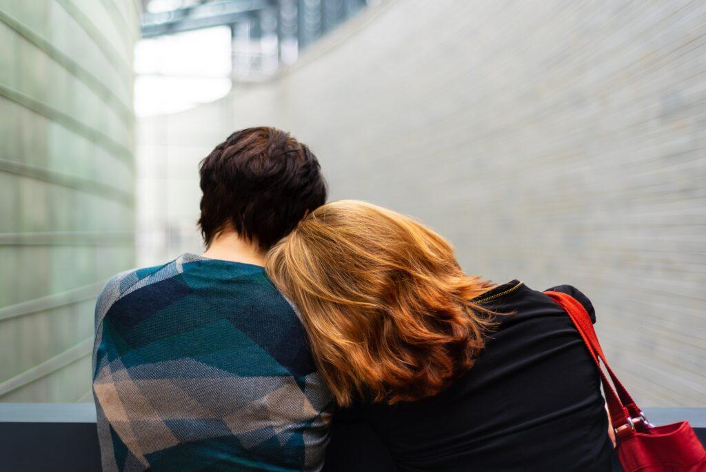 a photograph of two people, one man and one woman sitting side by side. the woman is resting her head on the man's shoulder. they are married